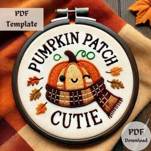 以下が含まれることがあります： 笑顔のかぼちゃが格子柄のスカーフを巻いている刺繍のフープアート。フープは茶色の木で、布は白地に「Pumpkin Patch Cutie」の文字が書かれています。