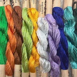 K&ouml;nnte beinhalten: Eine Sammlung farbenfroher Stickgarnkn&auml;uel. Die Garne sind in verschiedenen Farbt&ouml;nen erh&auml;ltlich, darunter Wei&szlig;, Gr&uuml;n, Orange, Braun, Gelb, Silber, Lila, Blau, T&uuml;rkis, Dunkelgr&uuml;n und Rot. Jedes Kn&auml;uel ist mit dem Wort "Embroidery Thread Fast Colour" beschriftet.
