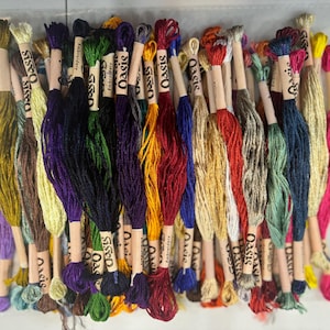 May include: A collection of 30 skeins of embroidery floss in various colors, including green, blue, red, yellow, and brown. Each skein is labeled "Oasis" and is wrapped in a white paper with a brown label.