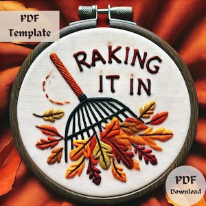 May include: An embroidered hoop featuring the phrase "Raking It In" in brown thread. A rake and colourful autumn leaves are stitched below the text. The words "PDF Template" and "PDF Download" are also visible.
