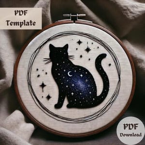 Könnte beinhalten: Ein Stickmuster einer schwarzen Katzensilhouette mit einem Sternenhimmel-Design. Die Katze sitzt mit ihrem Schwanz um den Körper gewickelt. Das Muster ist auf einem weißen Stoffhintergrund.