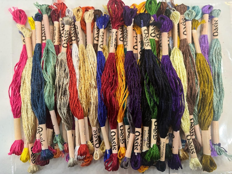 Puede incluir: Una colecci&oacute;n de carretes de hilo de bordar de colores con la palabra "Oasis" impresa en las etiquetas. Los carretes est&aacute;n dispuestos en fila y est&aacute;n listos para proyectos de artesan&iacute;a.