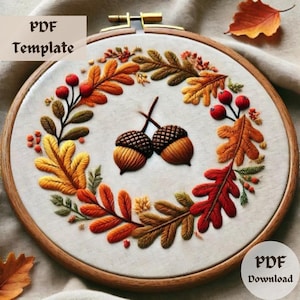 May include: Embroidered hoop art featuring a wreath of autumn leaves in shades of orange, red, and yellow, with two acorns in the center.