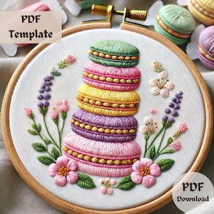 Op de afbeelding: Borduurwerk in een borduurring met een stapel kleurrijke macarons met een bloemenmotief. De macarons zijn roze, paars, geel en groen. De bloemen zijn roze, wit en paars.