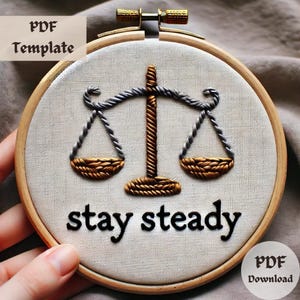 Puede incluir: Arte de bordado en aro con un diseño de balanza dorada y plateada y el texto "stay steady".