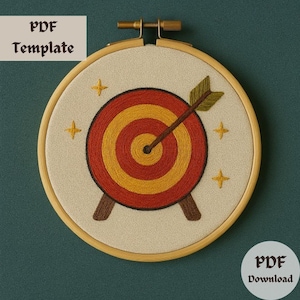 May include: A beige embroidery hoop with a red and yellow target with an arrow through the center. The target is surrounded by small yellow stars.