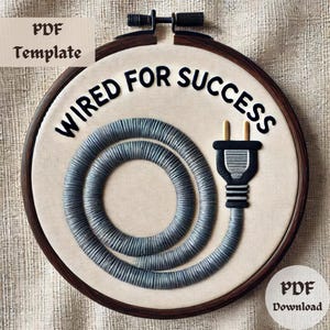 May include: A beige embroidery hoop with a black embroidery design of a power cord and the text "Wired for Success".
