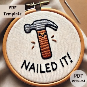 May include: Embroidered hoop art featuring a cartoon hammer with a smiling face and the text "NAILED IT!" in black thread. The hammer is embroidered in shades of brown and gray on a white fabric background.