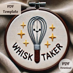 May include: A white embroidery hoop with a brown wooden frame. The hoop features a gray and silver embroidery of a whisk with a smiling face and the text "Whisk Taker" in brown thread. There are five yellow stars surrounding the whisk.