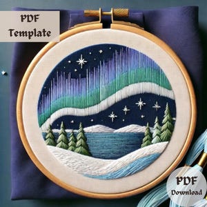 May include: Embroidered hoop art featuring a night sky with a green and blue aurora borealis, white stars, and a snowy landscape with a lake and trees. The hoop is made of wood and has a white background.