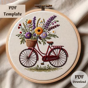 Puede incluir: Arte de bordado en aro con una bicicleta roja con una cesta de flores de colores. La bicicleta está sobre un fondo beige con un marco de aro de madera.