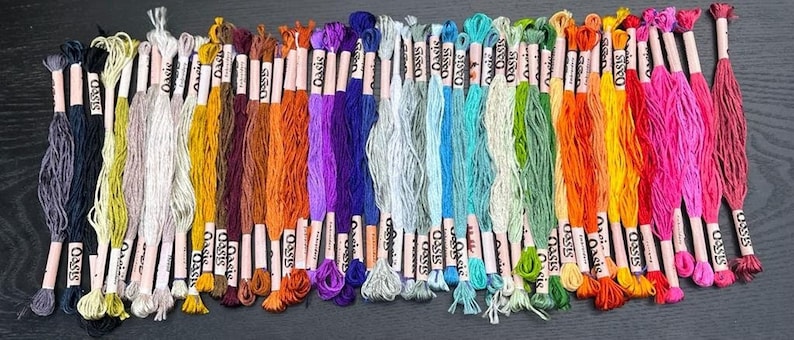 Puede incluir: Una colecci&oacute;n de 40 carretes de hilo de bordar en varios colores, incluyendo tonos de azul, verde, amarillo, naranja, rojo, rosa, morado, marr&oacute;n y gris. Cada carrete est&aacute; etiquetado con "Oasis".