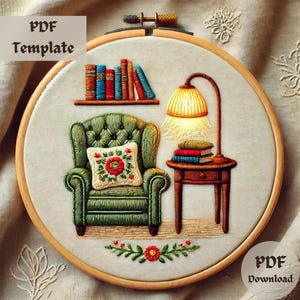 May include: Embroidered design of a cosy living room scene with a green armchair, a side table with books, and a lamp with a yellow shade. The design is stitched on a white fabric and framed in a wooden hoop.
