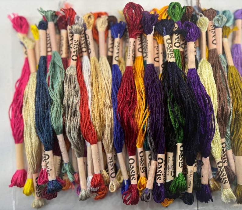 May include: A collection of colorful embroidery floss spools with the word "Oasis" printed on the labels. The floss is arranged in a variety of colors, including red, green, blue, yellow, and purple.