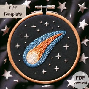May include: A wooden embroidery hoop with a black fabric background featuring a colorful comet with a white tail. The fabric is decorated with white stars and dots. The hoop is surrounded by a black fabric with white stars.