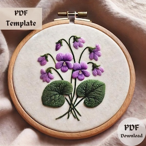 May include: A PDF template for embroidery featuring a design of purple violets with green leaves in a wooden embroidery hoop. The text "PDF Template" is at the top of the image and "PDF Download" is at the bottom.