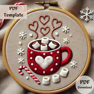 Könnte beinhalten: Stickerei auf einem Stickrahmen mit einer roten Tasse mit weißen Punkten und einem weißen Herzen, gefüllt mit heißer Schokolade und Marshmallows. Die Tasse ist von weißen Schneeflocken und einem Zuckerrohr umgeben.