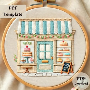 May include: Embroidered design of a bakery storefront with a blue awning, a door, and a window. The bakery has a sign that says "Shot" and is filled with cakes and pastries.