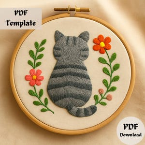 Op de afbeelding: Geborduurd kattenontwerp in een houten hoepel. De grijze tabby kat staat met de rug naar de kijker, omringd door groene bladeren en rode bloemen. De tekst "PDF Template" en "PDF Download" zijn zichtbaar.