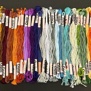 Puede incluir: Una colecci&oacute;n de 36 ovillos de hilo de bordar en varios colores, incluyendo tonos de verde, azul, naranja, morado y marr&oacute;n. Cada ovillo est&aacute; etiquetado con "Oasis".