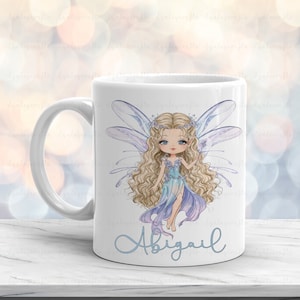 May include: White ceramic mug with a blue and purple fairy illustration and the name "Abigail" printed on the front.