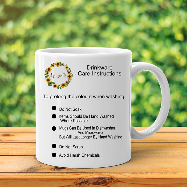 May include: White ceramic mug with a sunflower wreath design and the text "Zynlegerafts". The mug has black text that reads "Drinkware Care Instructions" and lists instructions for washing the mug, including "Do Not Soak", "Items Should Be Hand Washed Where Possible", "Mugs Can Be Used In Dishwasher And Microwave But Will Last Longer By Hand Washing", "Do Not Scrub", and "Avoid Harsh Chemicals".