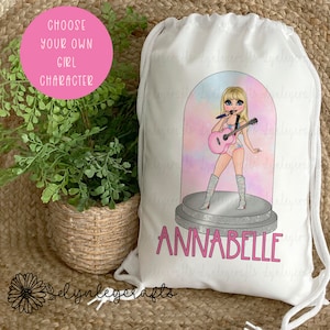 May include: White drawstring bag featuring a colourful illustration of a girl holding a guitar and singing into a microphone. The girl is wearing a pink and white outfit and has long blonde hair. The bag has the name "ANNABELLE" printed in pink letters.