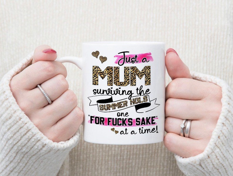 May include: White ceramic mug with a pink and black leopard print design. The mug reads "Just a MUM surviving the SUMMER HOLS one "FOR FUCKS SAKE" at a time!"