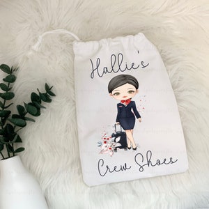 May include: White drawstring bag with a cartoon illustration of a flight attendant holding a suitcase. The bag has the text "Hallie's Crew Shoes" printed on it.