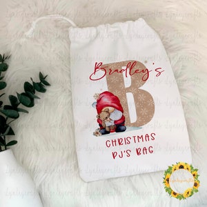 May include: White Christmas PJs bag featuring a red and white gnome holding a teddy bear. The bag has a brown letter B with snowflakes and the text "Bradley's Christmas PJs Bag".