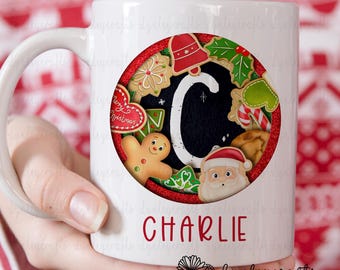 May include: White ceramic mug with a red circle design featuring a gingerbread man, candy canes, and a Christmas tree. The letter "C" is in the center of the circle, surrounded by other Christmas-themed cookies. The name "CHARLIE" is printed in red below the circle.
