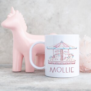 May include: White ceramic mug with a pink and blue unicorn carousel design and the name "Mollie" printed in pink.