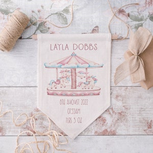 May include: A white canvas banner with a pink and blue unicorn carousel illustration. The banner reads "LAYLA DOBBS", "8TH AUGUST 2022", "07:55AM", and "7LBS 5 OZ".