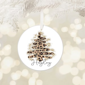 May include: White round Christmas bauble featuring a gold glitter leopard print Christmas tree and the name "Hayley" written in black cursive.