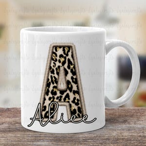 May include: White ceramic mug featuring a large letter A in a leopard print with gold glitter accents. The name Alice is written in cursive below the letter.