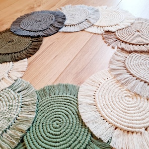 Könnte beinhalten: Ein Set runder, gehäkelter Untersetzer mit Fransen. Die Untersetzer sind in verschiedenen Farben, darunter Beige, Braun, Grün und Weiß.