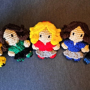 May include: Six crocheted dolls with different hair colors and outfits. The dolls are wearing a variety of colors, including yellow, green, red, blue, and brown.