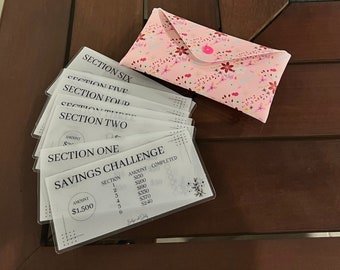 May include: A savings challenge game with six sections, each with a different amount to save. The game includes a pink envelope with a floral pattern and a button.