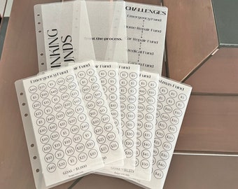 May include: A set of clear plastic sheets with black text and circles for tracking savings goals. The sheets are labeled with different fund names, such as "Emergency Fund", "Christmas Fund", and "Vacation Fund". Each sheet has a goal amount and a budget with Judy.