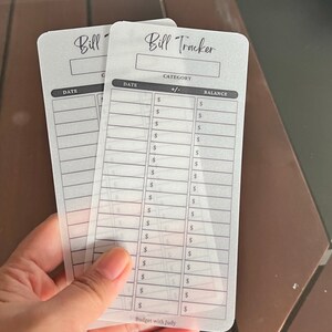 May include: Two clear plastic bill tracker sheets with black text. The top sheet has the title "Bill Tracker" and columns for "Date", "Category", "+/-", and "Balance". The bottom sheet has the title "Bill" and columns for "Date" and "Category".