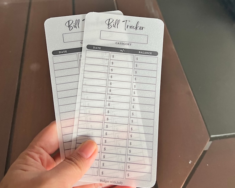 May include: Two clear plastic bill tracker sheets with black text. The top sheet has the title "Bill Tracker" and columns for "Date", "Category", "+/-", and "Balance". The bottom sheet has the title "Bill" and columns for "Date" and "Category".