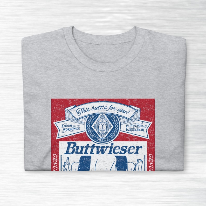 Peut inclure: Un t-shirt gris avec un graphique rouge, blanc et bleu d'une canette de bi&egrave;re parodique. La canette dit "Buttweiser" et "This butt's for you!"