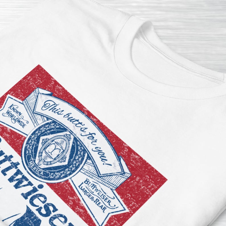 Peut inclure: Un t-shirt blanc avec un design de canette de bi&egrave;re Budweiser de style vintage. Le design pr&eacute;sente un sch&eacute;ma de couleurs rouge et bleu avec le texte "This Bud's for you!" et "Budweiser Larger Beer" dans une police de caract&egrave;res stylis&eacute;e.