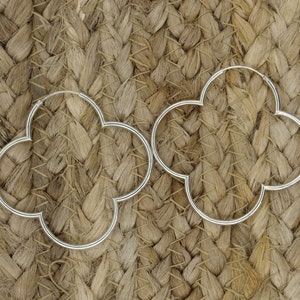 May include: A pair of silver hoop earrings shaped like a four-leaf clover.