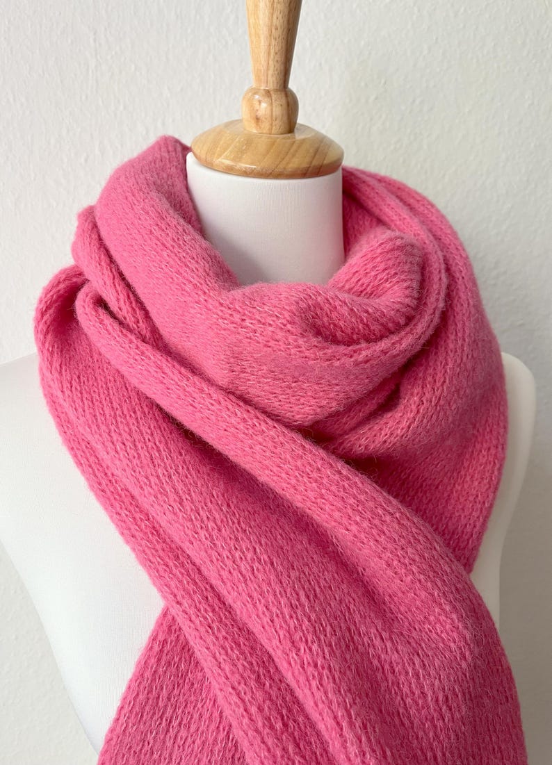 May include: A vibrant pink scarf, draped over a white mannequin head. The scarf is made of a soft, knitted material. The bright color and texture of the scarf are the focal points of the image.