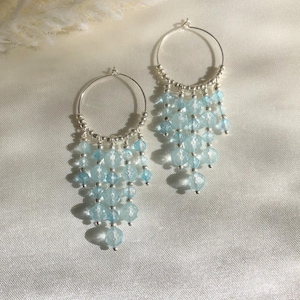 Peut inclure: Une paire de boucles d'oreilles créoles argentées avec un design en cascade de perles de verre bleu clair.