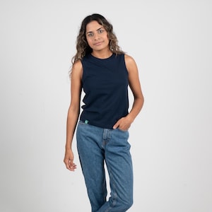 May include: A navy blue vest top. The top is made of a soft material and has a crew neck. The model is wearing blue jeans. The vest top has a small green logo on the bottom left.