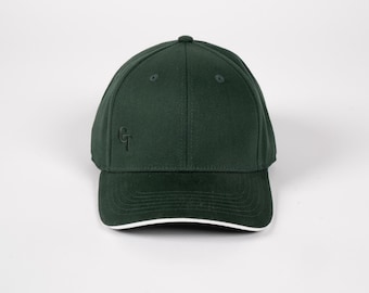 May include: A dark green baseball cap with a curved brim and a small embroidered logo on the side. The brim has a white trim. The cap is made of a textured fabric and has a button on top.