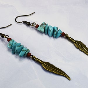 Puede incluir: Un par de pendientes de turquesa y bronce con un colgante de pluma. Los pendientes están hechos con piedras de turquesa y alambre de bronce. Las plumas son de color bronce claro.