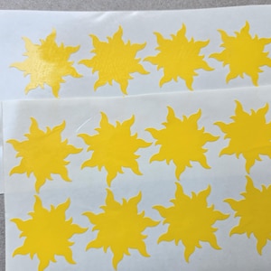 May include: Sheets of yellow sun-shaped stickers. Each sticker has a detailed, spiky design. The stickers are on a white backing, with several sheets visible. The stickers are a bright, cheerful yellow.